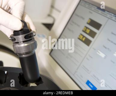 Un scientifique avec des gants de protection blancs tire un module d'une centrifugeuse à côté d'un écran d'ordinateur dans un laboratoire de céan équipé d'un laboratoire scientifique Banque D'Images