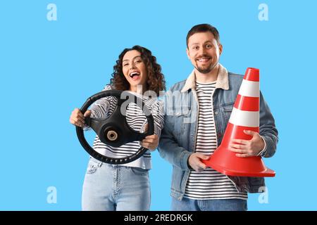 Jeune couple avec volant et cône de signalisation sur fond bleu Banque D'Images