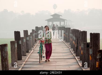 Une jeune femme birmane marchant sur le pont Ubein avec un vélo Banque D'Images