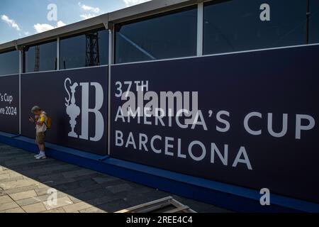 Barcelone, Espagne. 26 juillet 2023. Un touriste se réfugie de la chaleur sous le pavillon du magasin officiel de l'America's Cup Barcelona. Les installations de la compétition de voile American Cup Barcelona commencent à être visibles dans le port de Barcelone. Certaines des bases nautiques des équipes qui participeront au sport de compétition de voile le plus important arborent déjà les drapeaux de leur pays. Certaines équipes s’entraînent même déjà dans les eaux du port de Barcelone. Crédit : SOPA Images Limited/Alamy Live News Banque D'Images