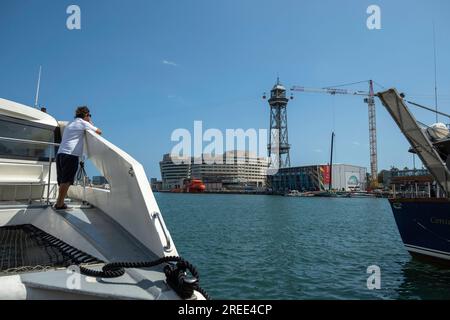 Barcelone, Espagne. 26 juillet 2023. Un homme observe depuis un bateau l’activité dans le pavillon Emirates Team New Zealand. Les installations de la compétition de voile American Cup Barcelona commencent à être visibles dans le port de Barcelone. Certaines des bases nautiques des équipes qui participeront au sport de compétition de voile le plus important arborent déjà les drapeaux de leur pays. Certaines équipes s’entraînent même déjà dans les eaux du port de Barcelone. Crédit : SOPA Images Limited/Alamy Live News Banque D'Images