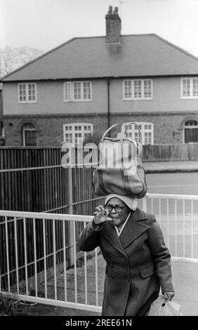 Faire un geste de main en colère de griffe, tirer le visage. Une femme britannique noire rentre chez elle du centre commercial Arndale portant ses achats dans un sac sur la tête. Gestuelle qu'elle n'est pas heureuse d'être photographiée. Wandsworth South London, Angleterre 1979 1970s UK HOMER SYKES Banque D'Images