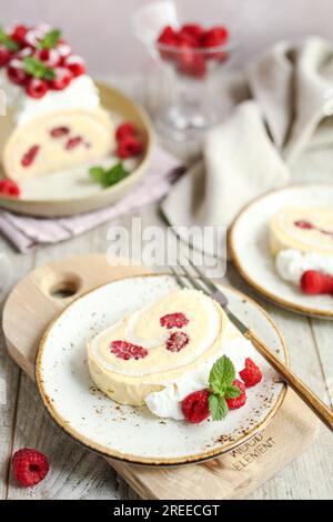 Roulade meringue framboise à la crème vanille, décorée de crème fouettée et de framboises fraîches. Table en bois et fond rose. Banque D'Images