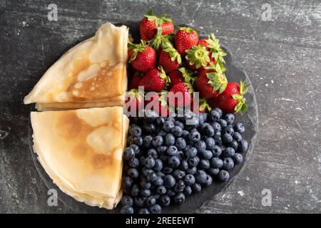photo de fines crêpes frites avec des fraises juteuses mûres et des myrtilles sur une assiette Banque D'Images