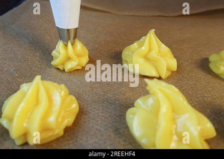 Cuisine souabe, préparation de mini-bouffées à la crème, presser la pâte à choux crue à travers un sachet à passepoil sur du papier sulfurisé, des échairs, des profiteroles, des pâtisseries bordées Banque D'Images