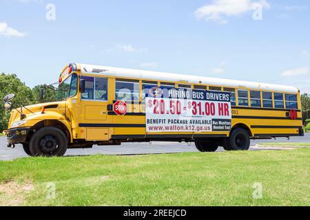 Monroe Géorgie, autobus scolaire jaune garé par l'autoroute, panneau de bannière, aide recherchée pour embaucher des chauffeurs de bus, paquet d'avantages, moniteurs nécessaires Banque D'Images