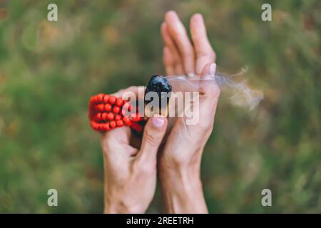 Vue d'angle de dessus d'un palo santo ou d'un bâton sacré d'arbre, brûlant avec la fumée d'arôme tenue par les mains de la femme sur le fond de la nature Banque D'Images