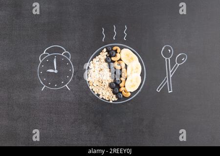 Flocons d'avoine avec noix et fruits. Concept petit déjeuner. L'assiette, la cuillère et l'horloge sont dessinées à la craie sur un tableau noir. Banque D'Images