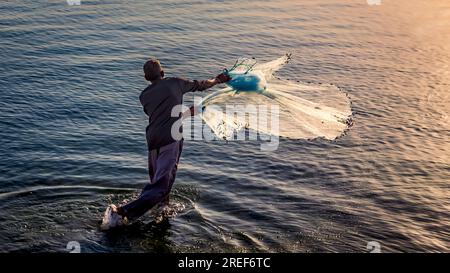 Un pêcheur jetant un filet de pêche pendant le lever du soleil à Al Khobar bord de mer en Arabie Saoudite. Banque D'Images
