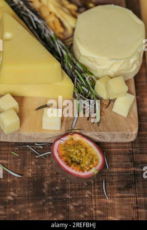 Fromage sur une planche de bois avec romarin et fruits de la passion. Triangles de fromage Mazdar, cubes de fromage gouda, chechil fumé Banque D'Images