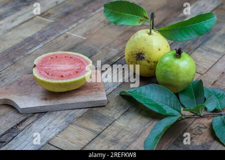 Goyave rouge frais avec des feuilles vertes sur fond en bois. Texture du bois et des feuilles de goyave. Banque D'Images