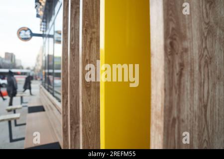 Un fragment de mur à l'intersection de plusieurs planches de couleur naturelle, une vue de la rue le long du mur. Des gens méconnaissables près du café. Photo de haute qualité Banque D'Images