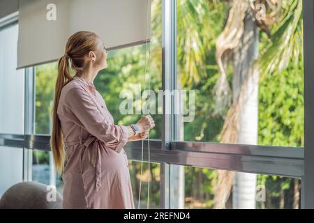 Portrait d'une jeune femme enceinte debout près de la fenêtre tenant les mains sur son ventre à la maison moderne avec l'espace de copie. Grossesse, maternité, espérance Banque D'Images