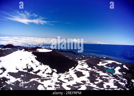 Un cindercone noir repéré avec de la neige et un lac Waiau immaculé près du sommet du Mauna Kea avec des nuages de haute altitude en arrière-plan. Banque D'Images