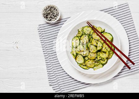 Sunomono, salade japonaise de concombres, tranches de concombres avec sauce asiatique de soja, vinaigre de riz, huile de sésame et sucre dans un bol blanc avec baguettes Banque D'Images