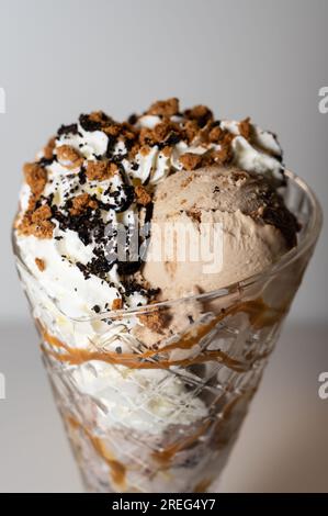 Biscuit Crunch gelato sundae servi dans un grand verre à sundae avec 3 boules de crème glacée, ainsi qu'une variété de sauces et garnitures. Banque D'Images