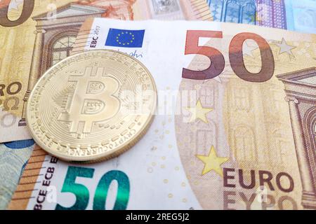 Gros plan sur une pièce Bitcoin en or au-dessus d'une pile de billets en euros. Banque D'Images