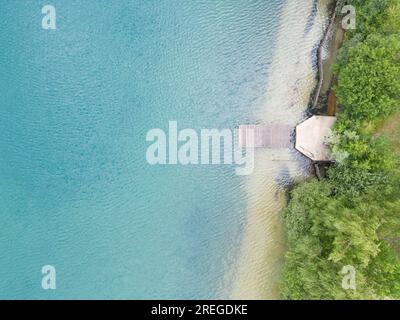 Une vue aérienne impressionnante d'une jetée en bois s'étendant gracieusement vers l'eau limpide et accueillante d'un lac serein. La tranquillité de la scène et la beauté naturelle du sable immaculé et de l'eau créent un visuel captivant et paisible. Sérénité aérienne : jetée en bois menant au lac Clear Water. Photo de haute qualité Banque D'Images