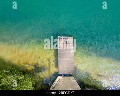 Une vue aérienne impressionnante d'une jetée en bois s'étendant gracieusement vers l'eau limpide et accueillante d'un lac serein. La tranquillité de la scène et la beauté naturelle du sable immaculé et de l'eau créent un visuel captivant et paisible. Sérénité aérienne : jetée en bois menant au lac Clear Water. Photo de haute qualité Banque D'Images