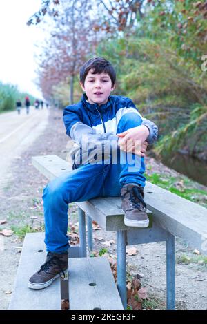 Jeune homme sérieux assis sur une balustrade en bois avec les bras autour des jambes Banque D'Images