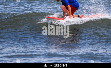 Un surfeur s'accroupissant bas sur un genou, chevauchant sur le sommet d'une petite vague tout en surfant à Gilgo Beach long Island. Banque D'Images