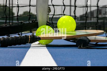 Gros plan de deux raquettes de pickleball et de deux balles jaunes à côté du filet sur un court de tennis. Banque D'Images