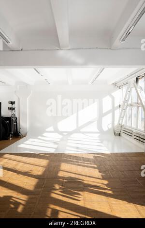 Nettoyez grand cyclorama blanc dans un studio photo avec une lumière du soleil et des ombres d'une immense fenêtre. Mur ordinaire vide studio photo. Banque D'Images
