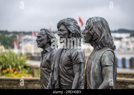 Statue sur la promenade Douglas érigée pour célébrer les Bee Gees nés sur l'île de Man Drapeau Manx en arrière-plan Banque D'Images