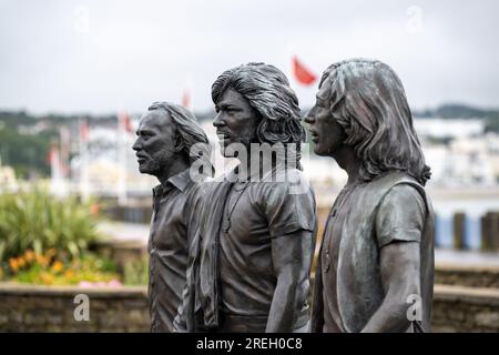 Statue sur la promenade Douglas érigée pour célébrer les Bee Gees nés sur l'île de Man Drapeau Manx en arrière-plan Banque D'Images