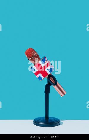 gros plan d'un microphone modelé avec le drapeau du royaume-uni, dans un support noir, placé sur une surface blanche, devant un fond bleu Banque D'Images