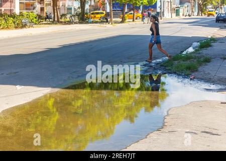 La Havane, Cuba, Une jeune cubaine traverse une rue vide de la ville. Il y a une grande flaque d'eau sale stagnante près du trottoir. Banque D'Images