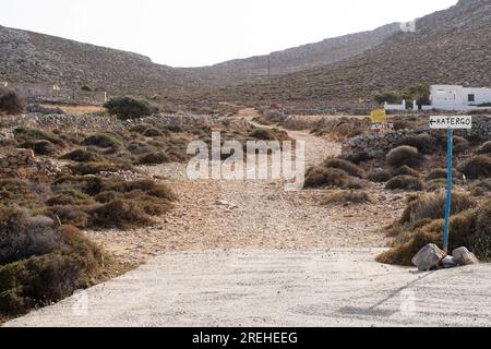 Chemin de gravier venant de la route bétonnée qui a un panneau manuscrit disant «KATERGO» avec une flèche pointant vers la gauche, menant entre deux bâtiments et Banque D'Images