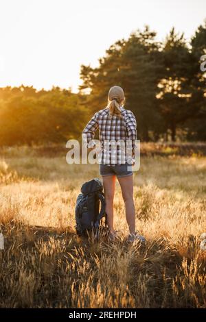 Femme avec sac à dos se repose dans la nature et profite du coucher de soleil d'été. Détendez-vous en randonnée sur un long sentier de trekking Banque D'Images