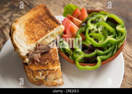 Toastie de pigeon, ou fonte, faite à partir de filets de pigeon blanc frits, de fromage et d'oignons rouges frits. Servi avec une salade mixte. Angleterre Royaume-Uni GB Banque D'Images