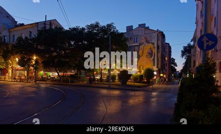 Rue la nuit à Sofia, Bulgarie, avec Street art d'une dame dans une robe jaune avec un casque sous le bras. Sofia, Bulgarie. 28 juillet 2023 Banque D'Images