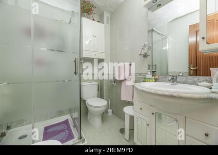 Salle de bain conventionnelle complète avec meuble lavabo avec miroir et lumières intégrées et cabine de douche avec cloisons en verre Banque D'Images