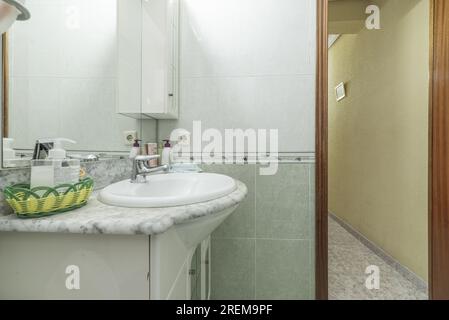 Salle de bain conventionnelle complète avec meuble lavabo avec miroir et éclairage intégré, carrelage vert et blanc séparés par une bordure Banque D'Images