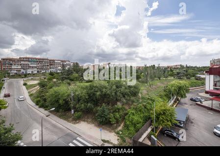 Beaux espaces paysagers d'un parc urbain avec des haies, des arbres et de l'herbe entourés de rues, de parkings et de bâtiments Banque D'Images