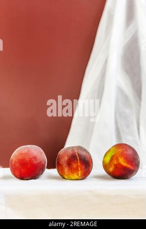 Quelques pêches rouges mûrissent en ligne sur un tissu blanc suspendu au mur Banque D'Images