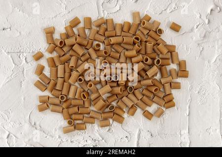 Tubes de pâtes de blé entier tranchées disposés en vrac sur une surface blanche rugueuse Banque D'Images