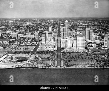 Miami, Floride c. 1930 regarder Flagler Street au centre-ville de Miami avec Miami Park et le front de mer au premier plan. L'hôtel McAllister se trouve sur le côté droit de Flagler Street, au premier plan. Banque D'Images