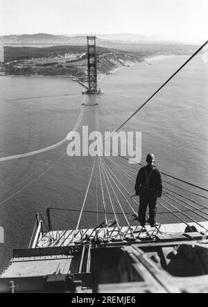San Francisco, Californie : 1935 Un homme debout sur les premiers câbles pendant la construction du Golden Gate Bridge avec le Presidio et San Francisco en arrière-plan. Banque D'Images