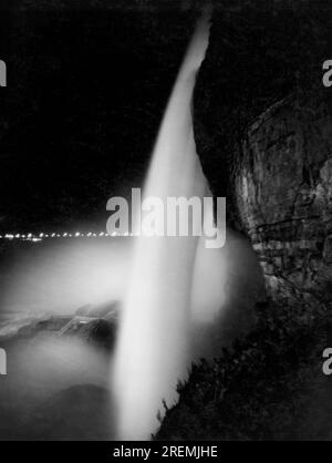 Niagara Falls, New York : c. 1923 vue des chutes centrales avec la lueur des chutes américaines derrière elles. Le pont international est vu illuminé au loin. La photographie a été prise de nuit avec l'illumination de 1 500 000 000 lampes à arc de bougie du côté canadien. Banque D'Images