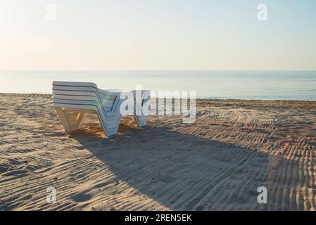 Chaises longues pliées en plastique sur une plage déserte au bord de la mer. Banque D'Images