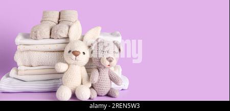 Pile de vêtements de bébé, chaussettes et jouets tricotés sur fond lilas avec espace pour le texte Banque D'Images