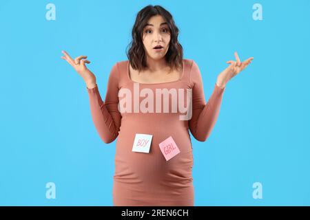 Confondu jeune femme enceinte avec des mots GARÇON et FILLE sur des papiers sur fond bleu Banque D'Images