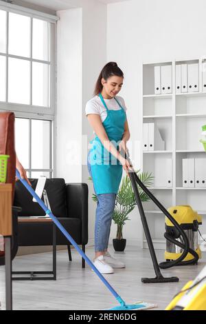 Une femme concierge passe l'aspirateur sur le sol du bureau Banque D'Images