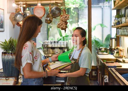 Jeune serveuse vietnamienne travaillant avec la machine de check out et les clients dans le café Banque D'Images