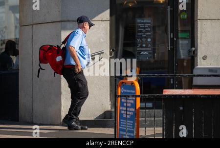 Royal Mail Postman ou Post Person livrant des lettres et du courrier à des locaux commerciaux dans la zone urbaine en Angleterre, Royaume-Uni. Profession. Banque D'Images
