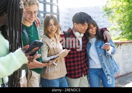 Un groupe d'étudiants universitaires multiculturels debout, interagissant, serrant, avec des sacs à dos et des téléphones portables dans la cour de l'université. Banque D'Images